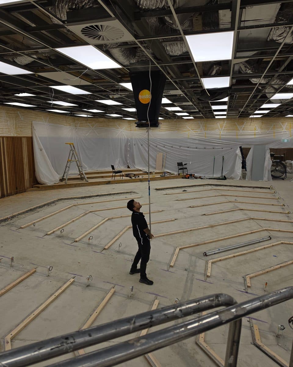 One technician measuring an exposed-grid ceiling outlet at height with ENGIC's extension base